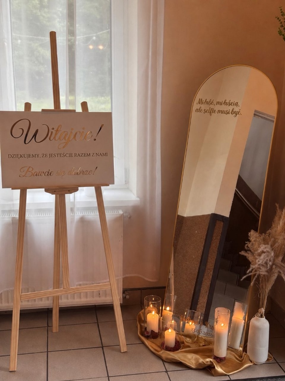 Lustro dekoracyjne przy wejściu na salę — tabliczka powitalna „Witajcie!”, personalizowany napis na lustrze, świece i trawa pampasowa