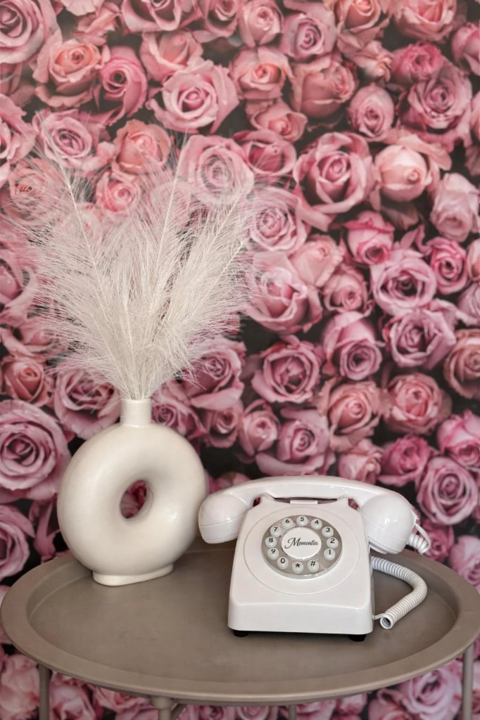 Telefon życzeń Momentia — biały aparat na tle ściany z róż